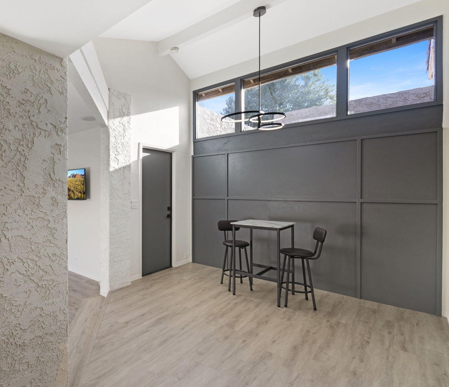 Finished charcoal paneled accent wall with clerestory windows above and a bistro table in front