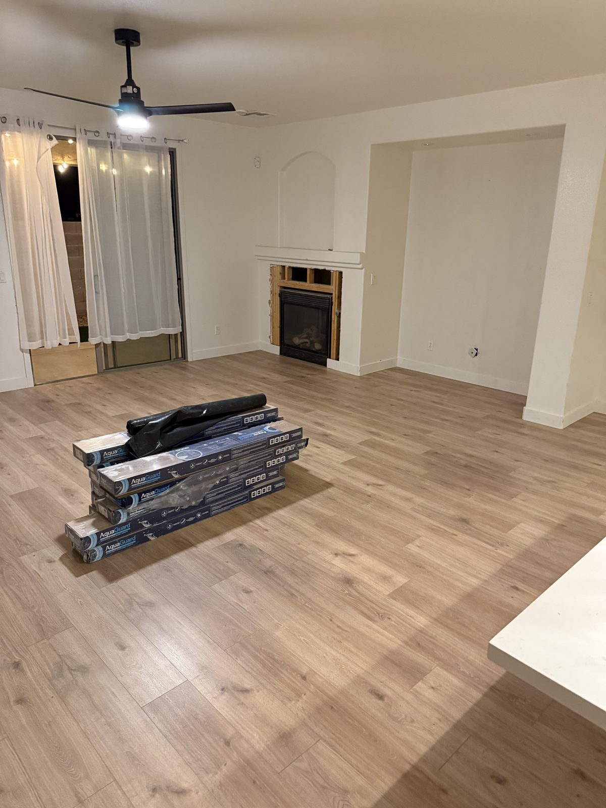Same living room with light wide plank waterproof flooring running continuously through both rooms and new baseboards installed
