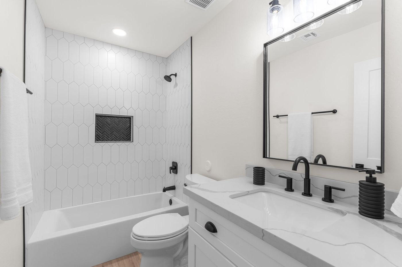 Renovated guest bathroom with white tile tub surround, quartz vanity, and black fixtures
