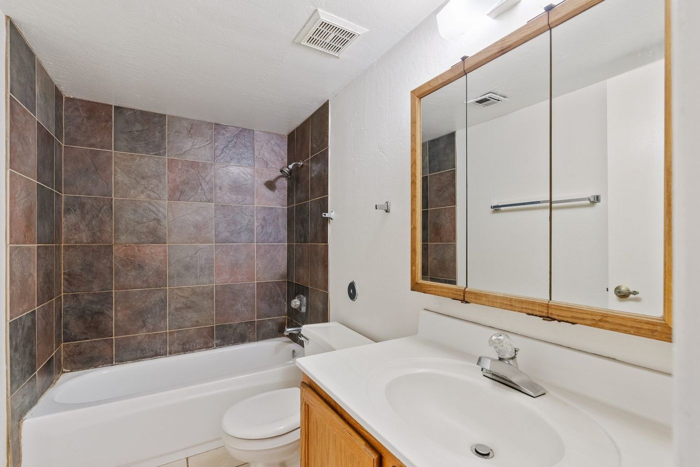 Guest bathroom with brown tile tub surround and oak framed mirror before renovation