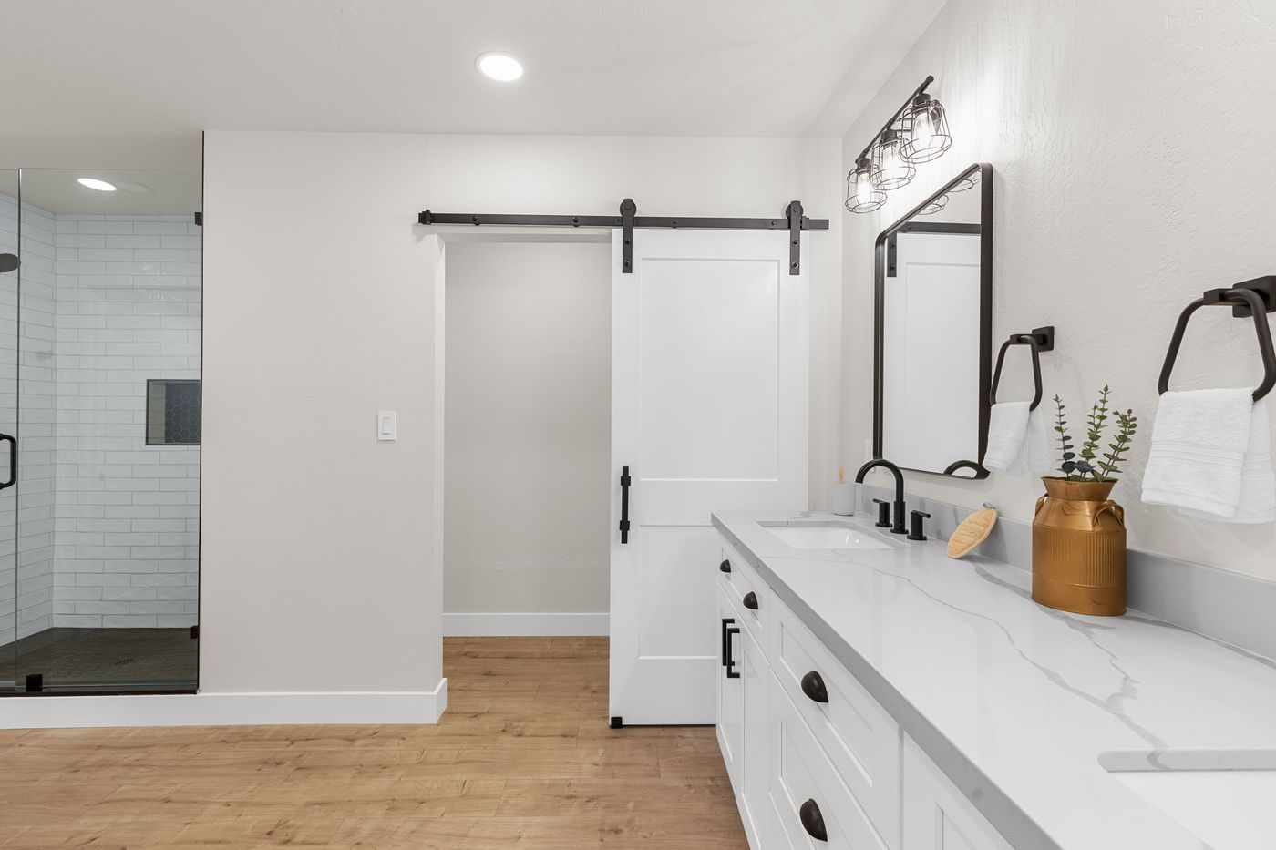 Renovated primary bathroom with double quartz vanity, black fixtures, and a barn door