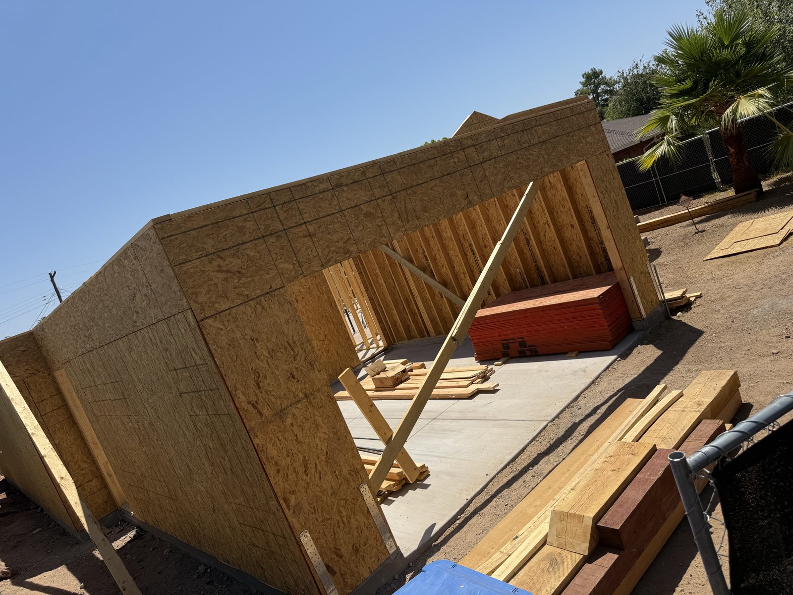 Framed and sheathed garage walls with braced walls and stacked lumber on the new slab