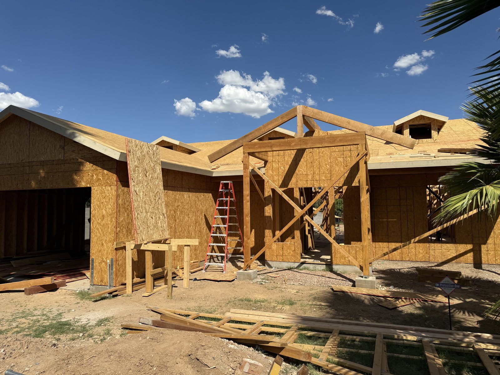 Framed home with roof sheathing and heavy timber entry trusses under an Arizona sky
