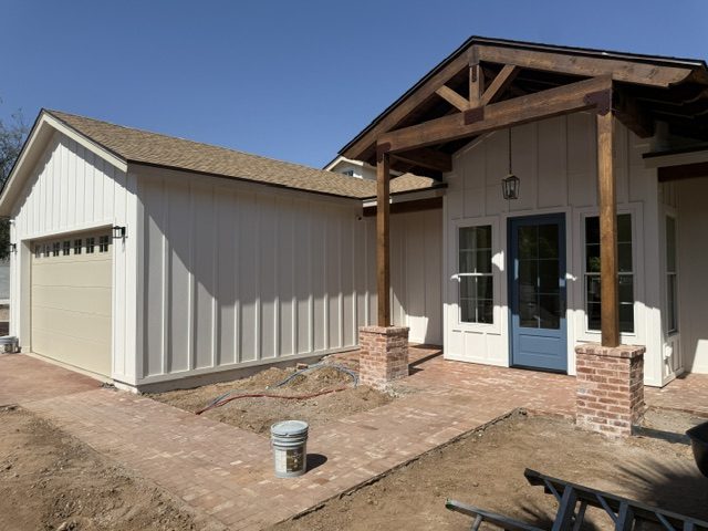 Completed exterior with white board and batten siding, timber posts on brick bases, and a blue front door