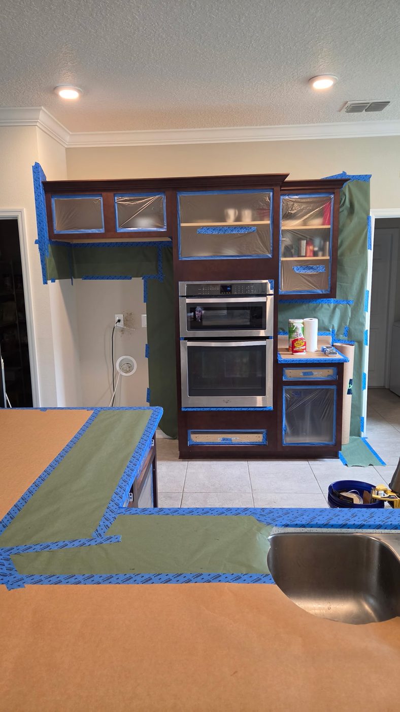 Cabinet boxes masked with paper and tape while appliances and counters stay protected